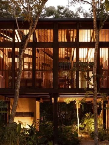 Holzhaus mit großen Fenstern und beleuchtetem Inneren bei Nacht im Wald.