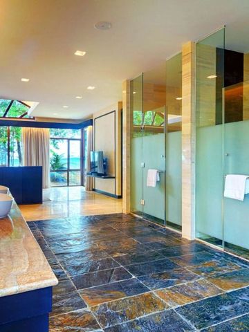 Luxuriöses Badezimmer mit Glaswänden und Natursteinboden mit Meerblick.