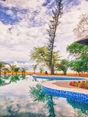 Infinity-Pool mit Meerblick und Palmen am Horizont unter wolkenlosem Himmel.
