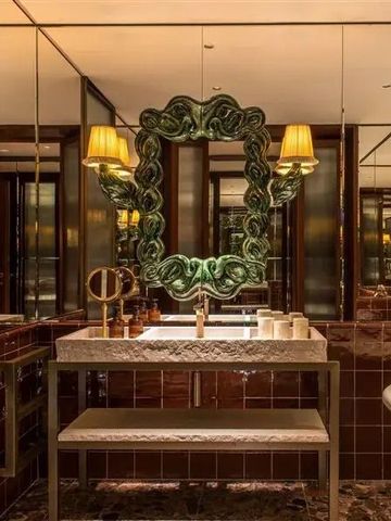 Elegantes Badezimmer mit kunstvollem Spiegel und warmer Beleuchtung.