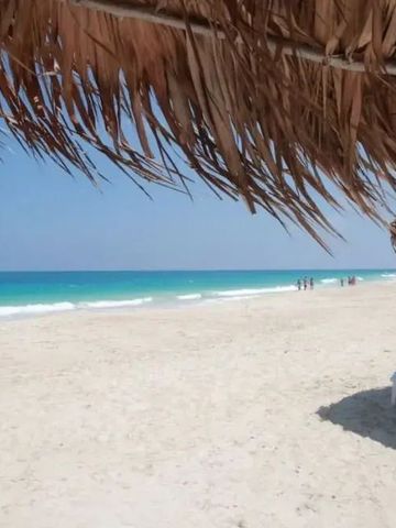 Blick auf den weiten Sandstrand und das türkisblaue Meer unter Strohdach