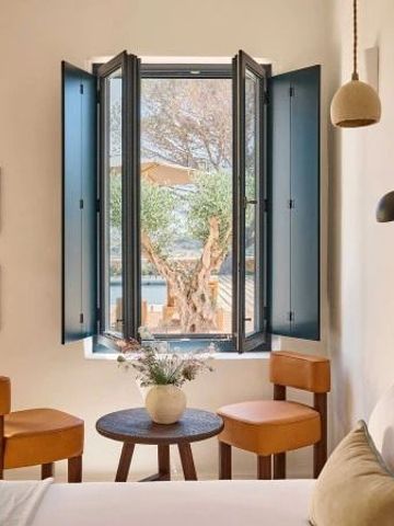 Zimmerdetail mit offenem Fenster, gemütlicher Sitzecke und Pflanzen.