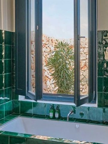 Freistehende Badewanne mit grün gefliesten Wänden und Blick aus dem Fenster