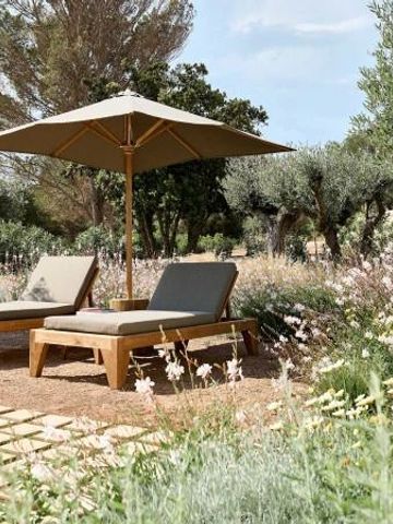 Zwei Sonnenliegen unter einem Sonnenschirm in einem blühenden Garten