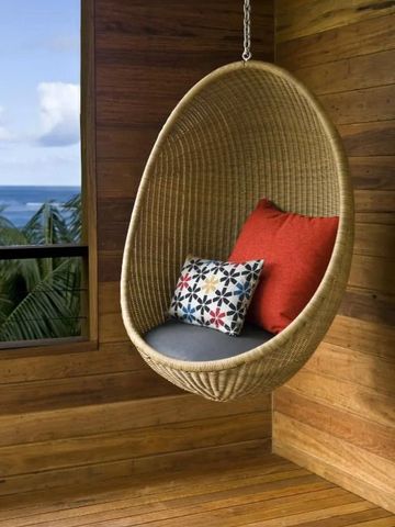 Runder Hängesessel mit bunten Kissen und Meerblick durch ein Fenster