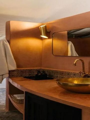 Elegantes Badezimmerzelt mit goldener Waschtischarmatur und Lehmwänden