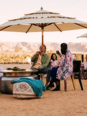 Gruppe von Menschen sitzt unter Sonnenschirmen in einer Wüstenlandschaft.