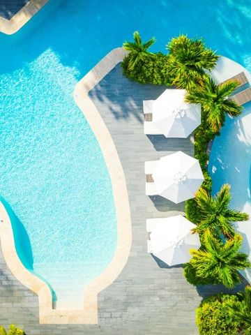 Luftaufnahme eines Pools mit weißen Sonnenschirmen und Palmen