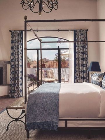 Elegantes Schlafzimmer mit Himmelbett und Kaminöffnung zu sonniger Terrasse.