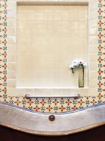 Charmante Badewanne vor kunstvoll gefliester Wand mit dezenter Blumenverzierung