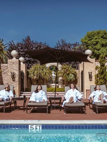 Gäste entspannen auf Liegestühlen am Pool mit umgebenden Pflanzen und blauen Himmel