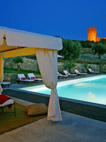 Nachtansicht eines eleganten Pools mit Liegestühlen und beleuchteter Burg im Hintergrund