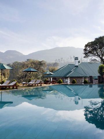 Großer Pool mit Liegestühlen und grüner Landschaft im Hintergrund.