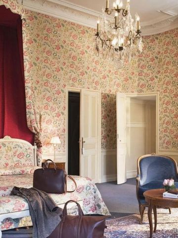 Elegantes, floral gestaltetes Hotelzimmer mit Kronleuchter und Kamin.