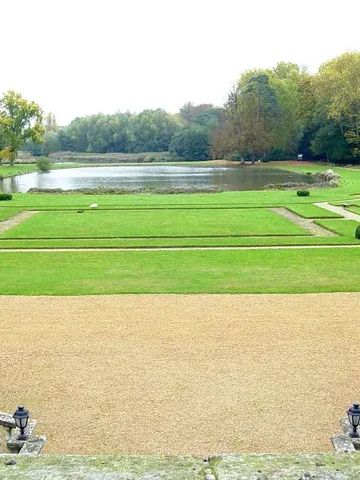 Großer, gepflegter Garten mit See und symmetrischen Wegen.