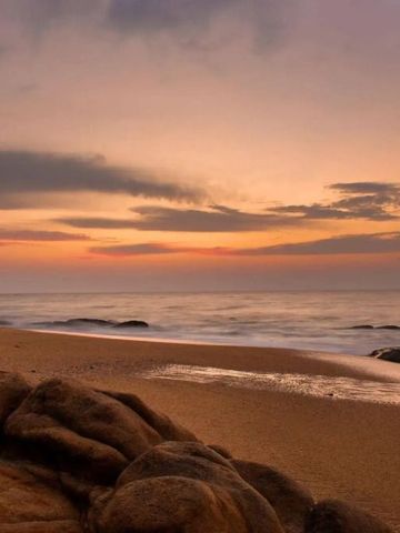 Sandstrand bei Sonnenuntergang mit ruhiger Meeresbrandung.