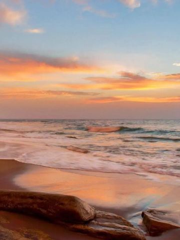 Sonnenuntergang am Strand mit sanften Wellen und klarem Himmel.