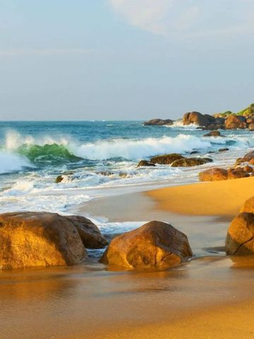 Wellen brechen gegen Felsen bei sonnigem Wetter am Strand.