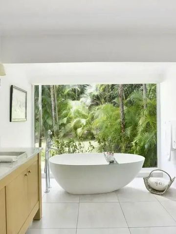 Modernes Badezimmer mit freistehender Badewanne und Glaswand Blick auf Palmen