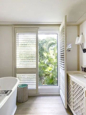 Helles Badezimmer mit freistehender Badewanne und Blick auf Palmen.