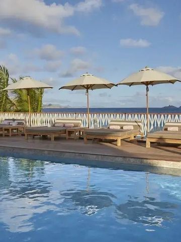 Poollandschaft mit Liegen und Sonnenschirmen unter blauem Himmel.