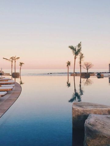 Infinity-Pool mit Blick auf den Ozean bei Sonnenuntergang umgeben von Palmen