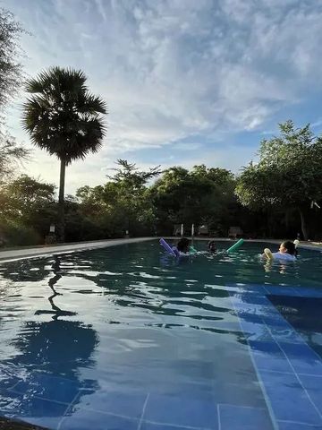 Großer Swimmingpool mit Menschen und Bäumen im Hintergrund bei Sonnenuntergang.