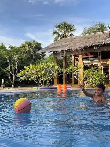 Vater und Sohn spielen mit einem Ball im Pool neben einem strohgedeckten Pavillon.