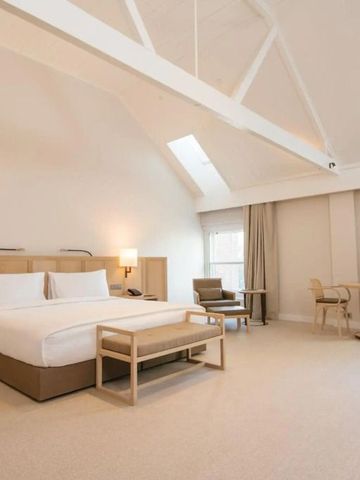 Geräumiges Hotelzimmer in neutralen Farben mit großem Bett und Sitzbereich