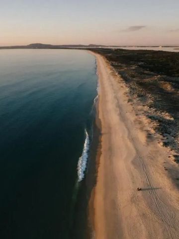Weitläufiger Sandstrand bei Sonnenuntergang mit ruhigem Meer