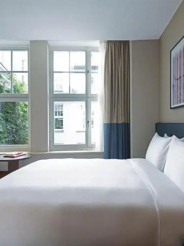 Helles Hotelzimmer mit großen Fenstern, Doppelbett und stilvollem Interieur
