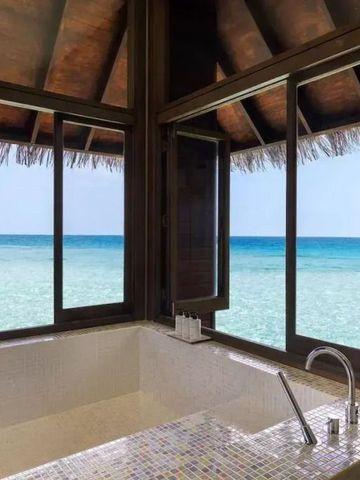 Badewanne mit Blick aufs türkisblaue Meer durch große Fenster