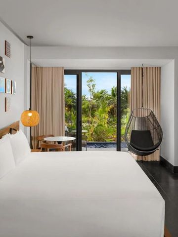 Modernes Hotelzimmer mit großem Bett, Holzdetails und Blick auf tropische Vegetation