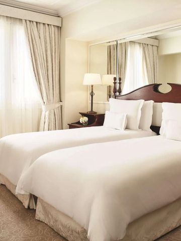 Zwei Einzelbetten in einem hellen Zimmer mit Vorhängen und Spiegel.