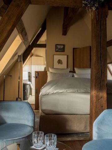 Gemütliches Dachzimmer mit freiliegenden Holzbalken und blauen Sesseln.