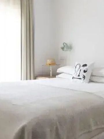 Schlichtes Gästezimmer mit weißem Bett und natürlichem Licht durch ein Fenster.