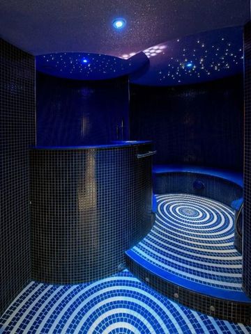 Stimmungsvoller Spa-Bereich mit blauer Beleuchtung und Wandmosaik.