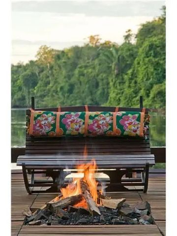 Gemütliche Sitzbank mit Kissen und Feuerstelle im Freien mit Blick auf bewaldetes Ufer