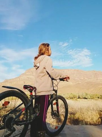 Person mit Fahrrad vor einer malerischen Bergkulisse unter klarem blauen Himmel