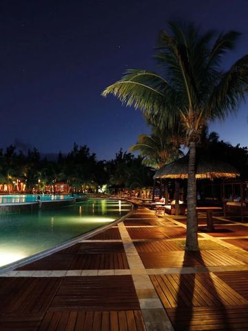 Beleuchteter Poolbereich bei Nacht mit Palmen und Holzterrasse