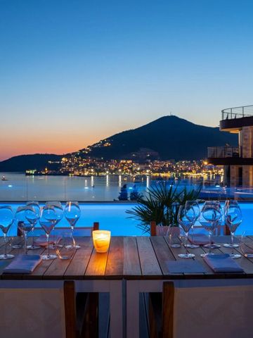 Abendstimmung auf der Terrasse mit Blick auf den beleuchteten Küstenort und den Infinity-Pool