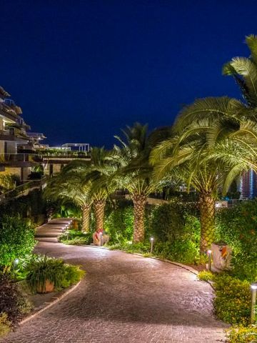 Beleuchteter Gartenweg mit Palmen vor dem nächtlichen Hotelgebäude