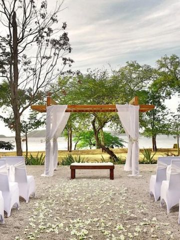 Hochzeitseinrichtung am Strand mit weißem Drappagen und Stühlen