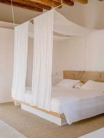 Modernes Schlafzimmer mit weißen Vorhängen und hölzernem Bett im Hotel Es Racó d'Artà