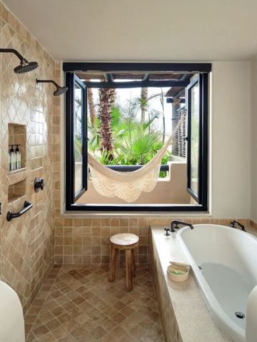 Helles Badezimmer mit Badewanne und Hängematte neben einem Fenster mit Palmenblick