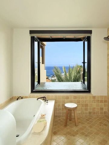 Badewanne im Badezimmer mit Fensterblick auf den Ozean und tropische Pflanzen