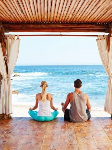 Personen meditieren in einem Pavillon mit Blick aufs Meer