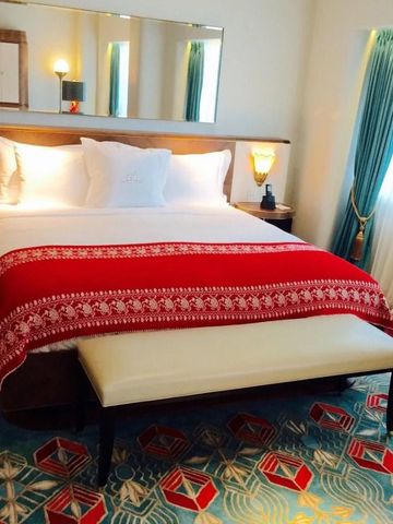 Hotelzimmer mit großem Bett, luxuriöser roter Decke und geometrischem Teppich