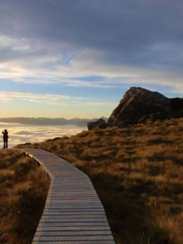 Holzsteg führt über goldenes Gras mit spektakulärem Himmel im Hintergrund.
