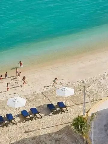 Luftaufnahme eines Strandes mit türkisfarbenem Wasser und Sonnenliegen
